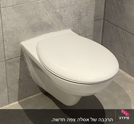 אסלה תלויה לבנה מותקנת על קיר אריחים אפור בחדר שירותים